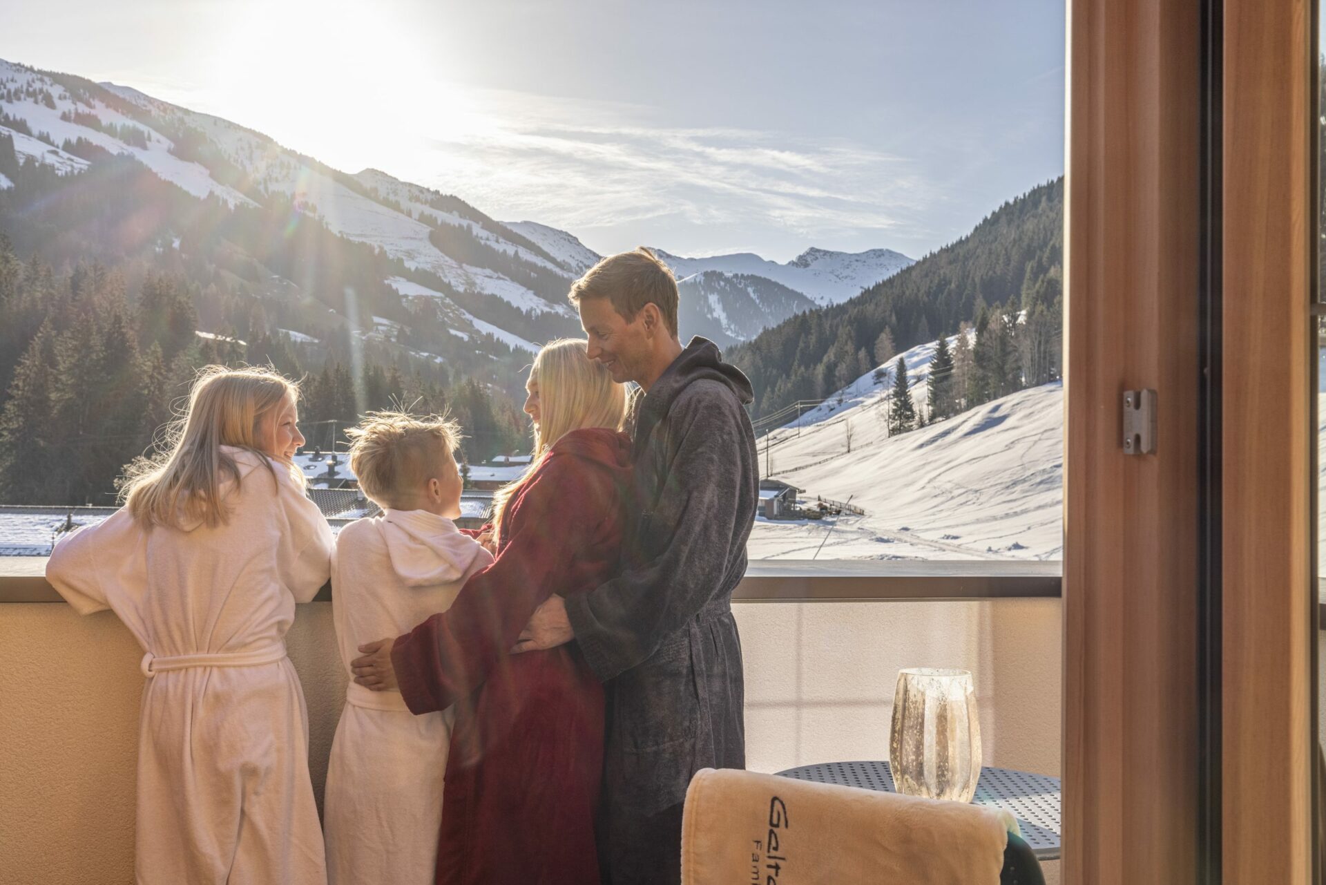 Eine Familie genießt im Bademantel Impressionen auf einem Balkon mit Blick auf die Berge.