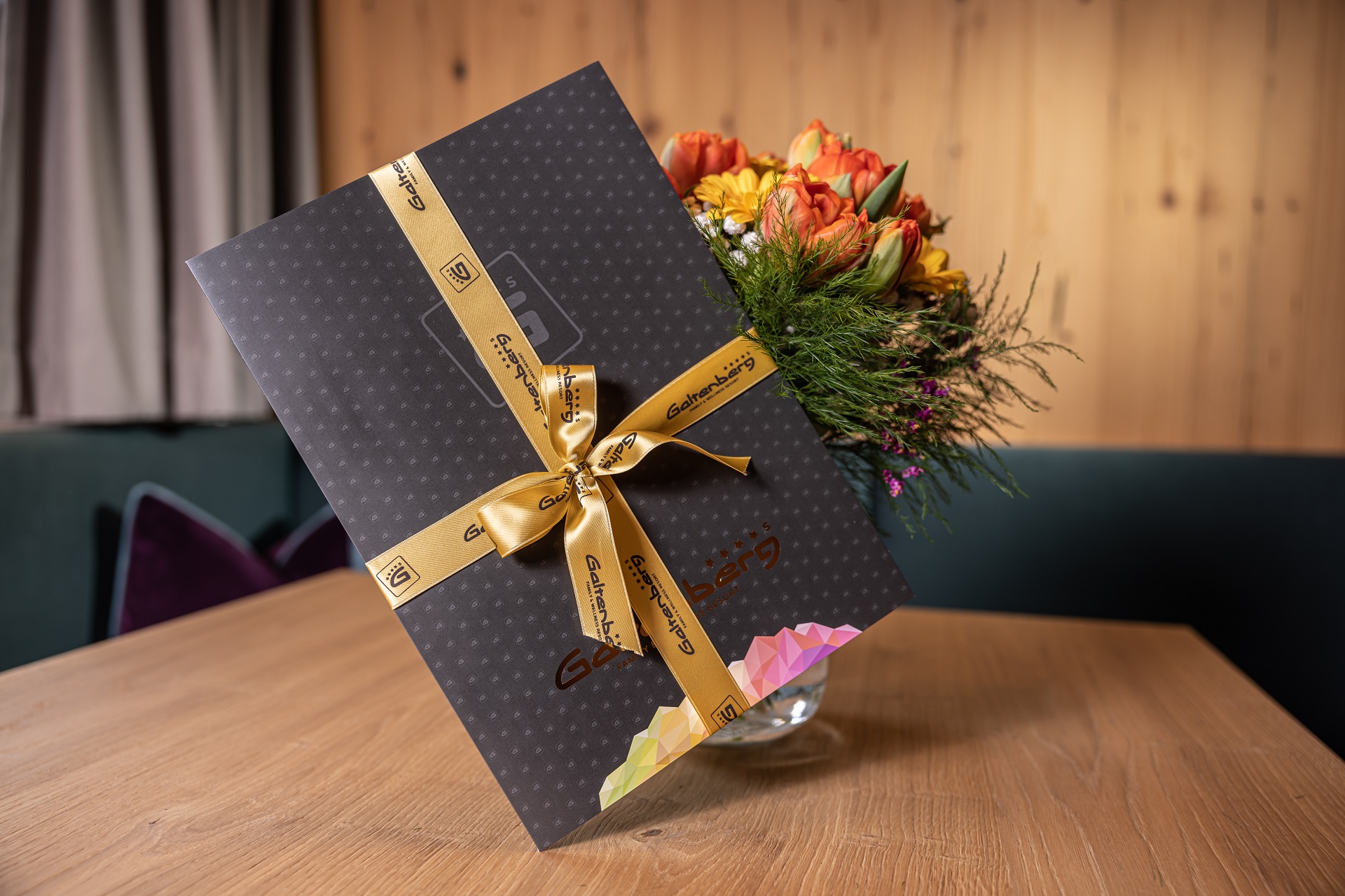 A black and gold gift box with a bouquet of flowers and vouchers.