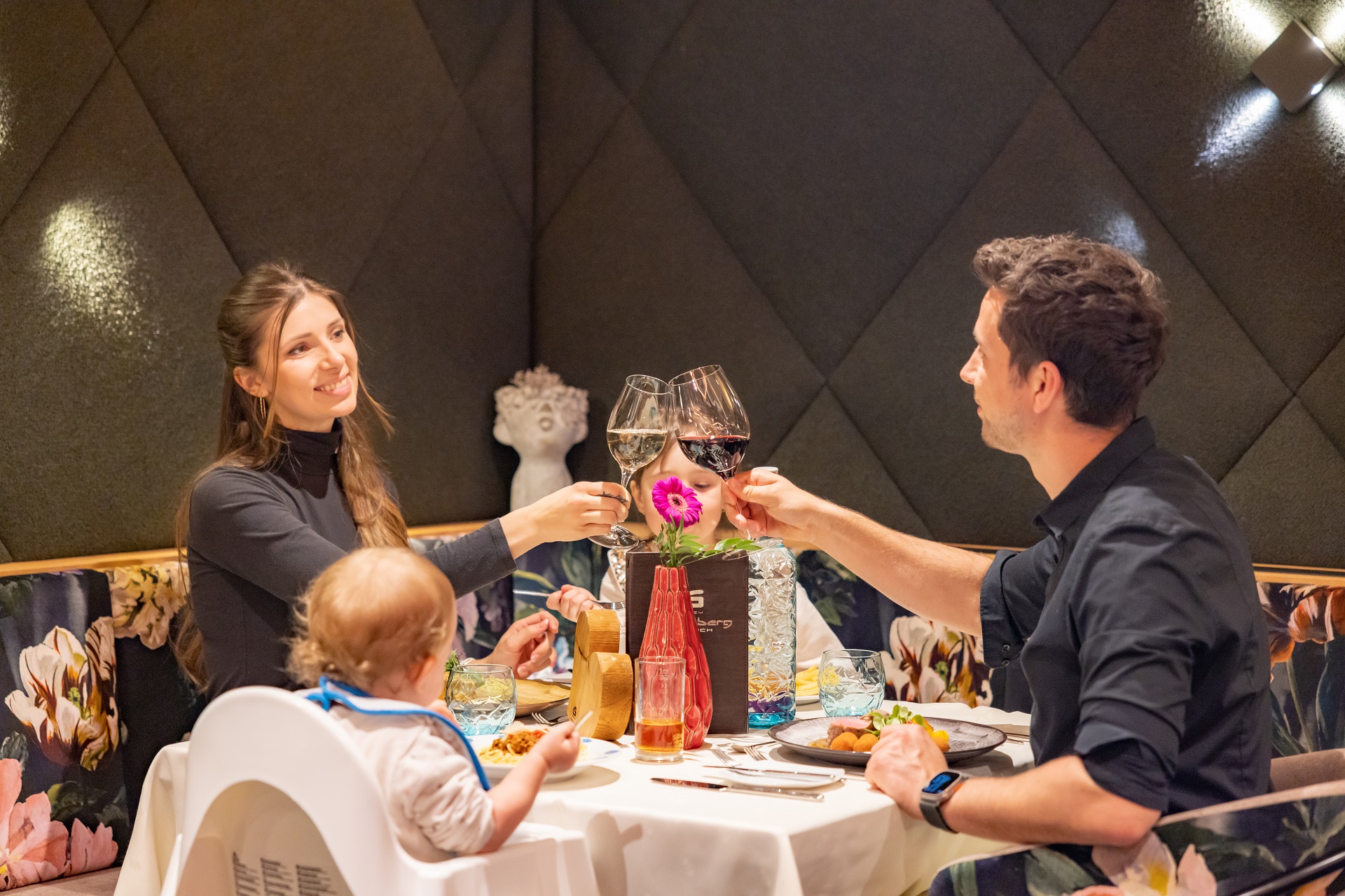 A couple with a baby enjoying dinner at a restaurant table.