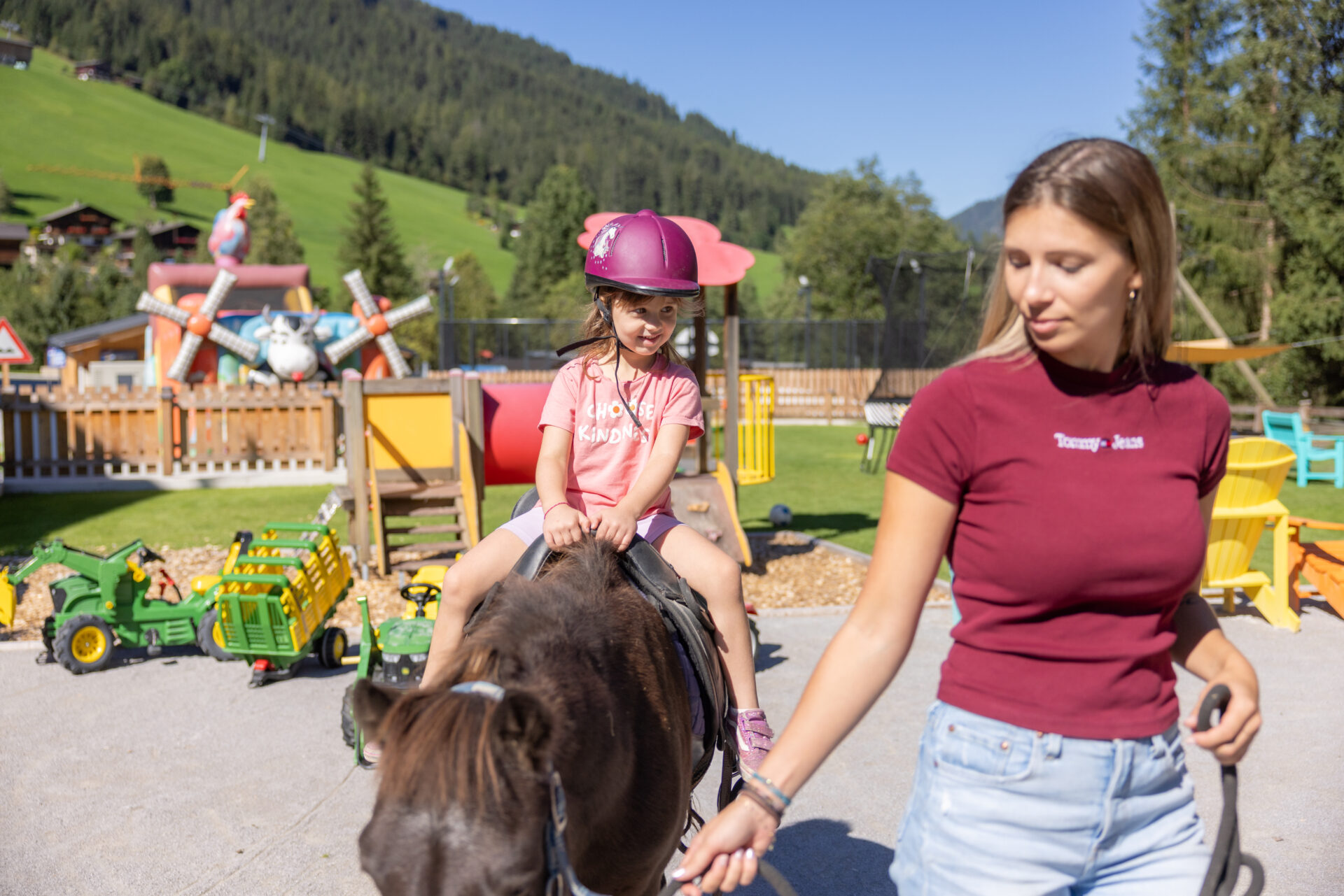Eine Frau reitet auf einem Pferd mit einem kleinen Mädchen im Hintergrund.