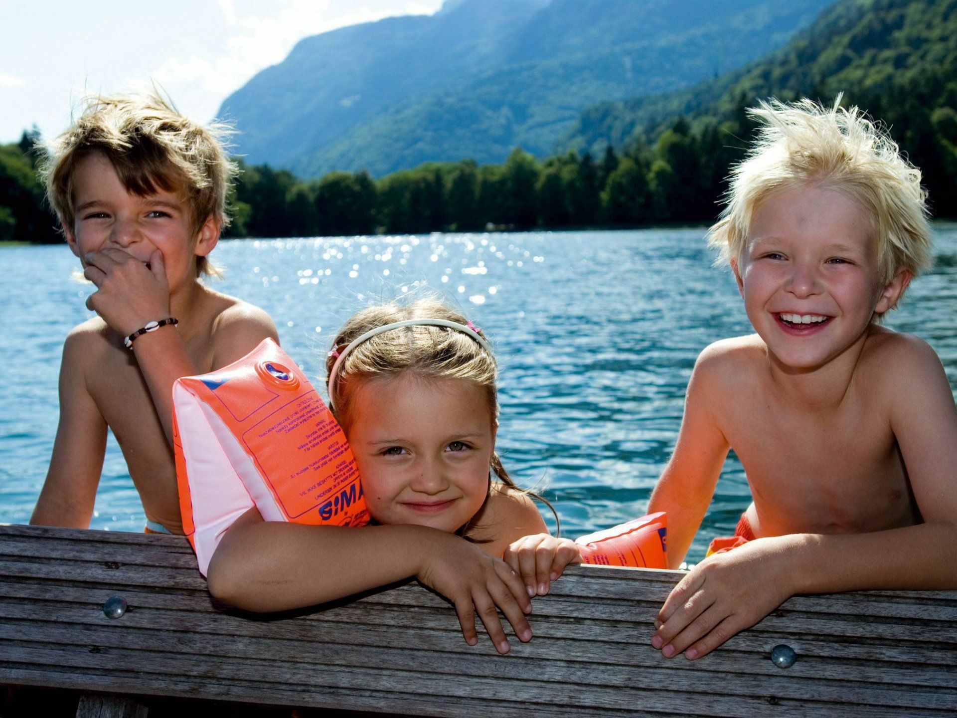 Kinder auf einer Holzbank an einem See.