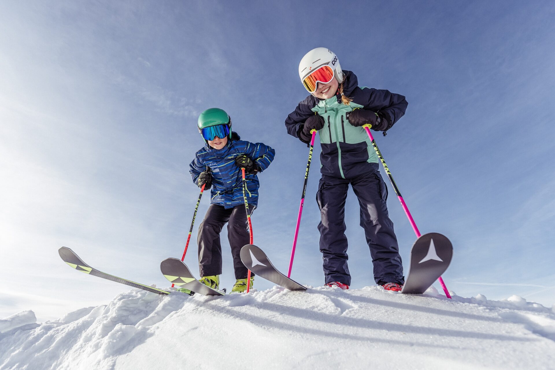 Zwei Kinder stehen mit Skiern auf einem Berg.