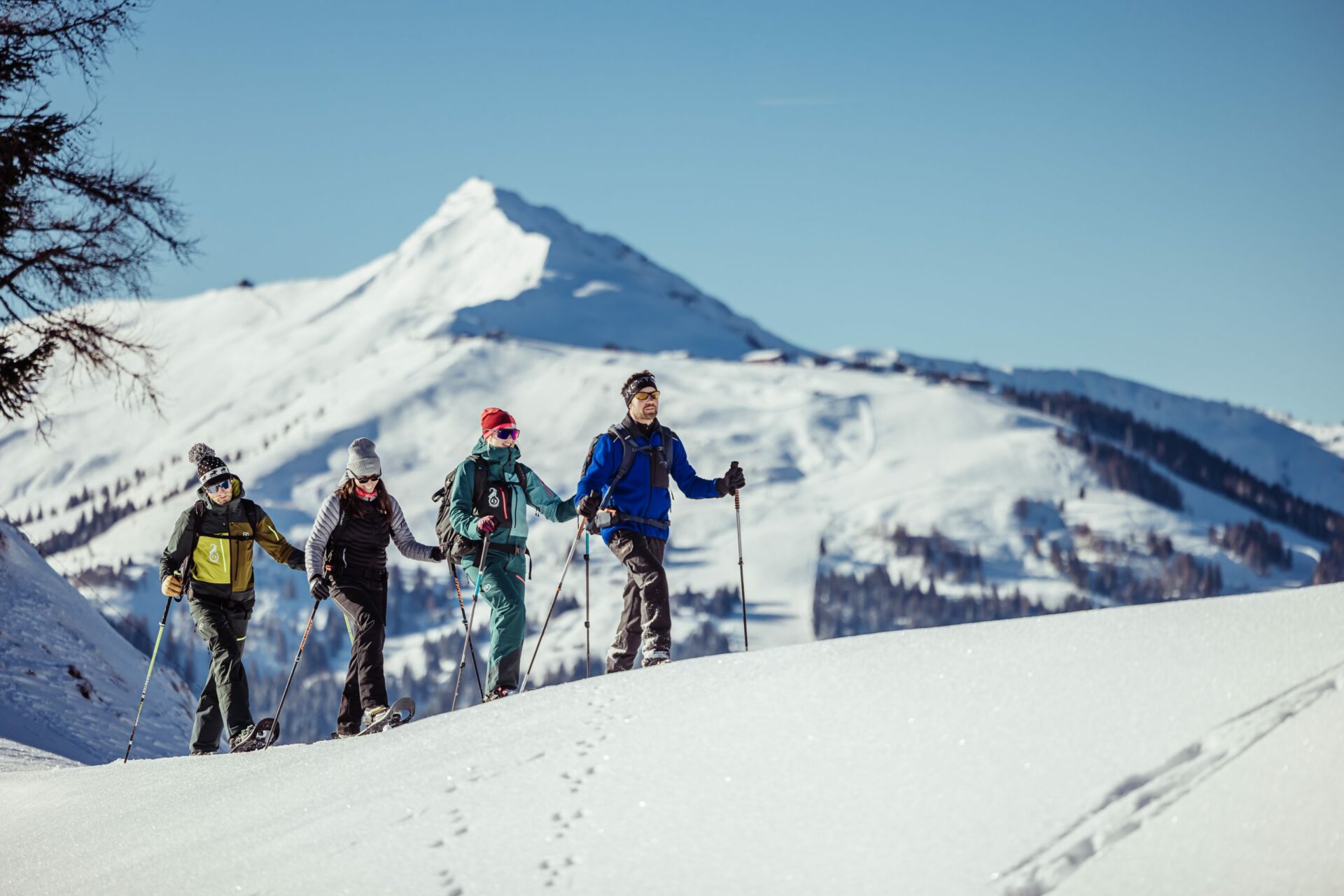 Menschen gehen mit Skiern durch den Schnee, im Hintergrund schneebedeckte Berge.