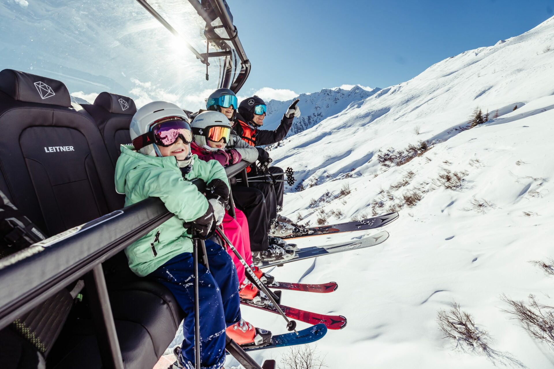 Familie mit Skiern sitzt in einem Sessellift auf dem Weg zum Berggipfel.