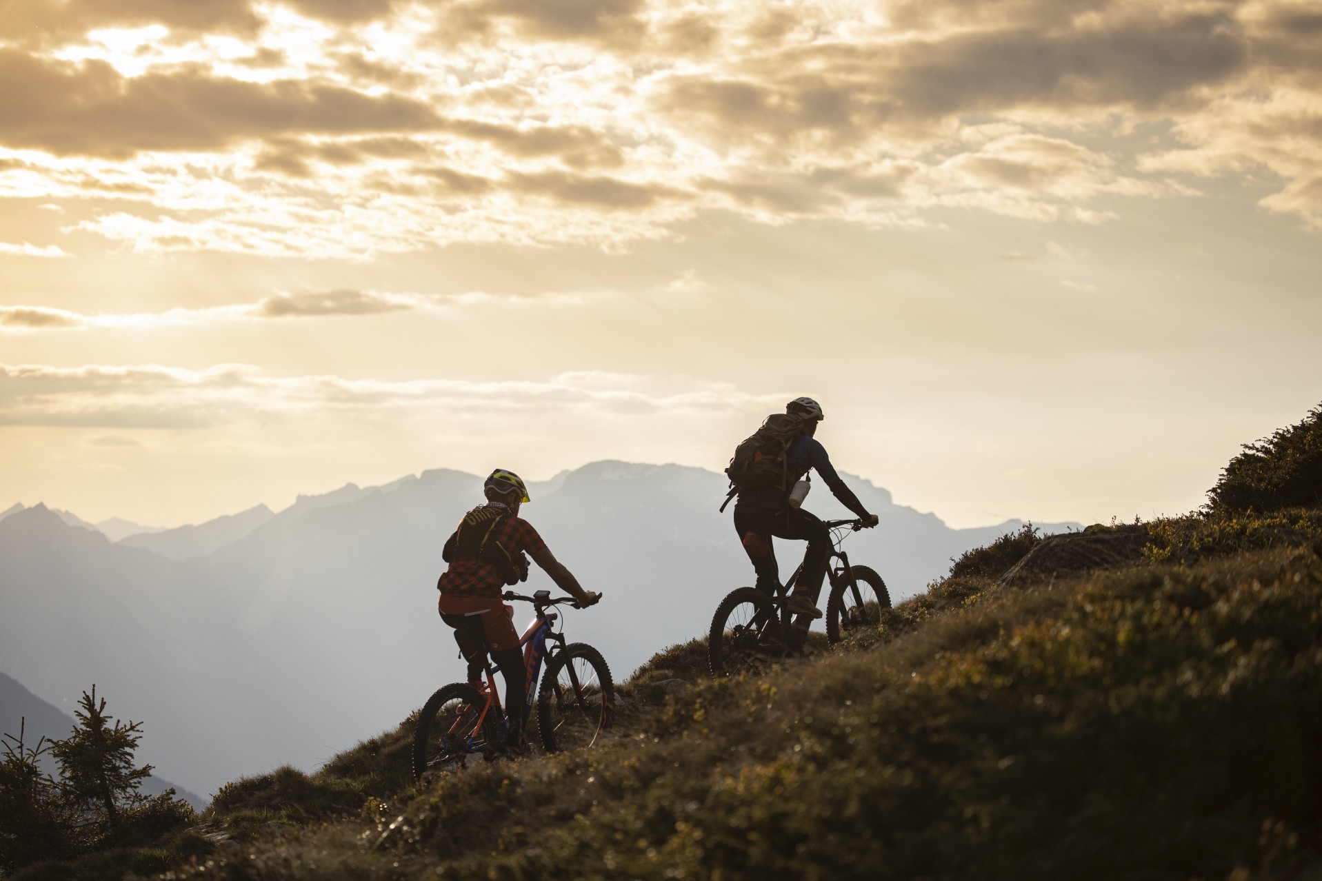 Zwei E-Biker fahren bei Sonnenuntergang einen Berg hinunter.