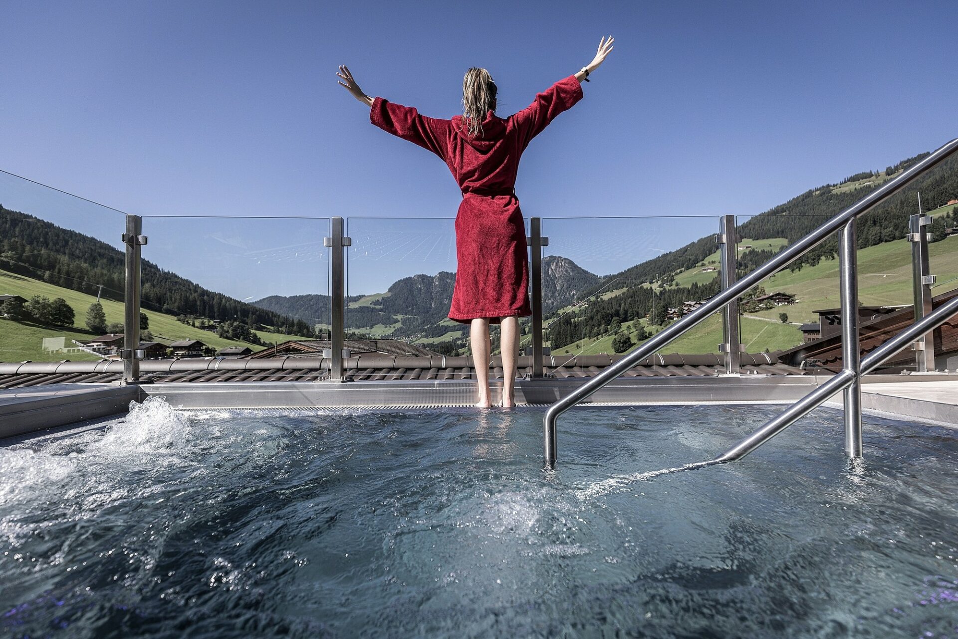 Eine Frau in einem roten Bademantel genießt Wellness in einem Whirlpool im Freien.