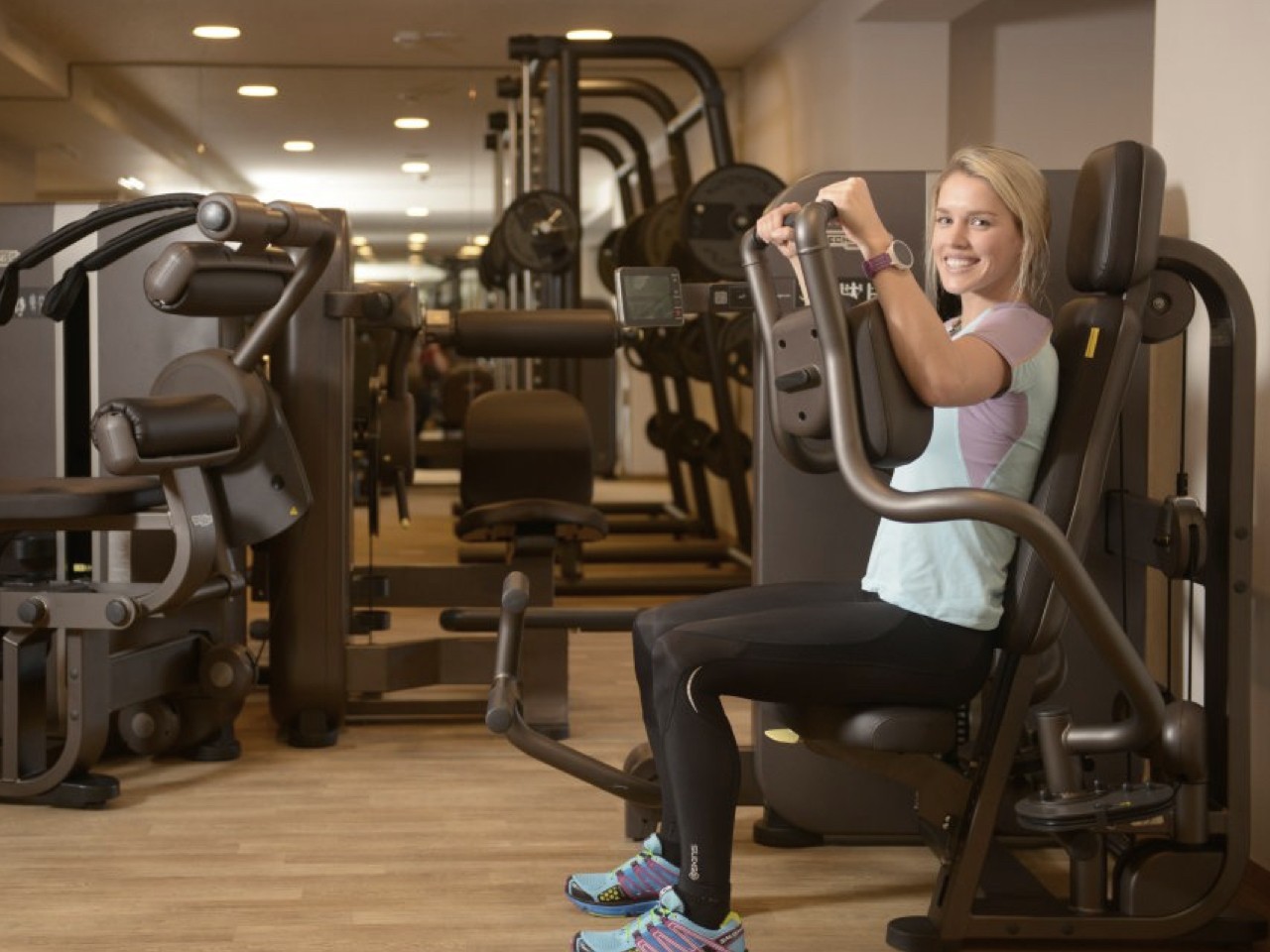 Eine Frau trainiert im Sommer an einem Gerät in einem Fitnessstudio.